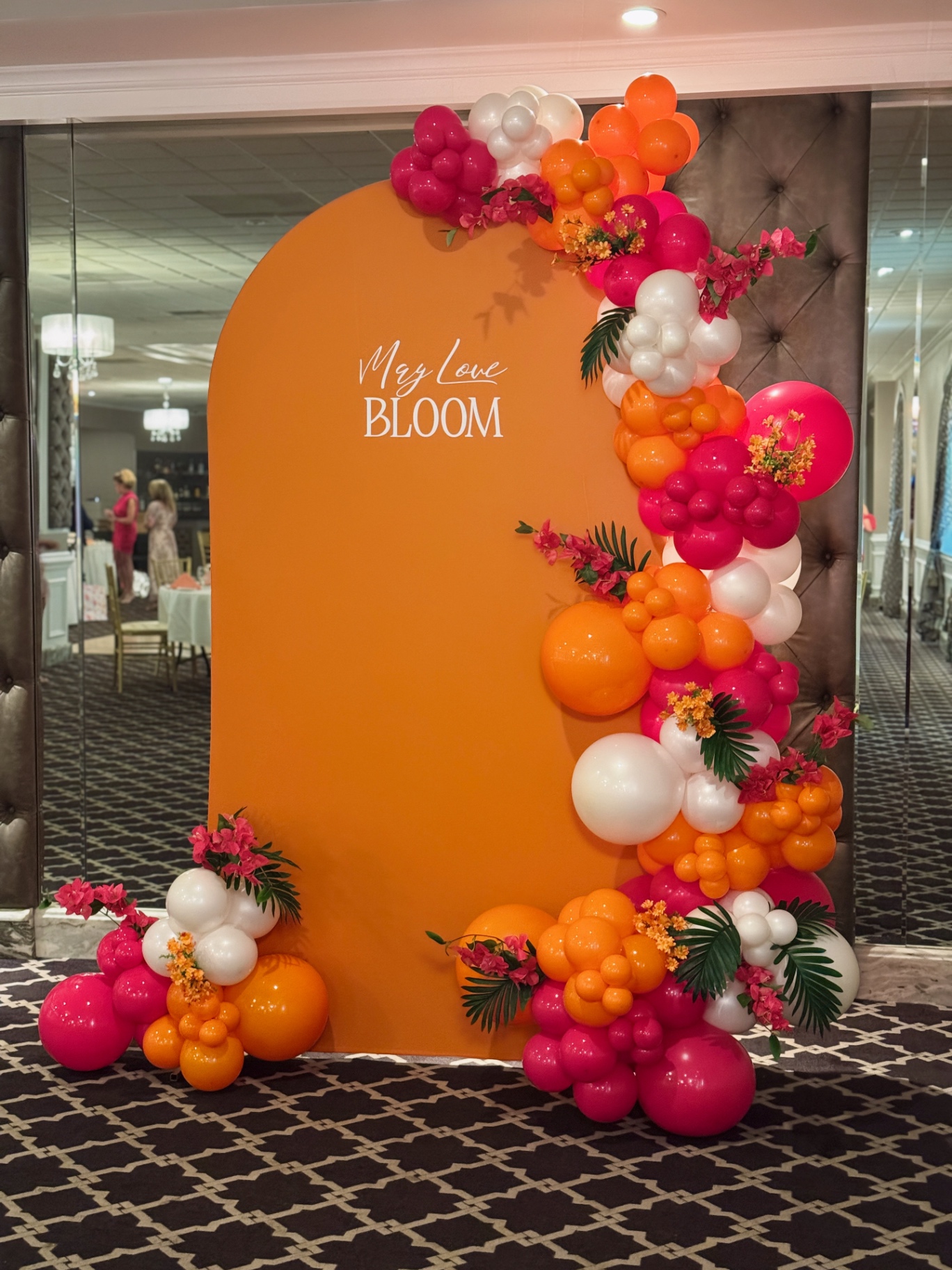 Vibrant orange arch with pink and orange balloon garland and tropical florals
